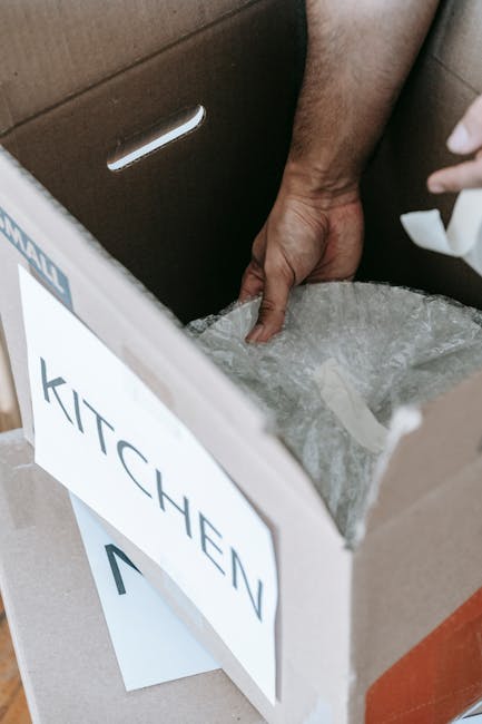 The image shows a room with a concrete floor that has a slightly reflective surface. In the foreground, there is an open cardboard box containing a pile of crumpled, grey fabric or clothing. Behind th